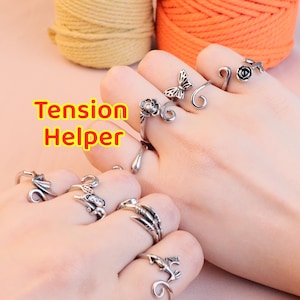 Op de afbeelding: Zilverkleurige ringen met diverse ontwerpen, waaronder een vlinder, roos en draak, worden op vingers getoond. De tekst "Tension Helper" is zichtbaar. De ringen zijn waarschijnlijk verstelbaar en bedoeld voor knutselen of andere activiteiten.