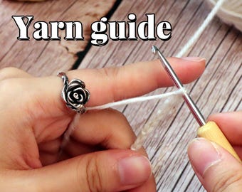 Peut inclure: Gros plan sur des mains travaillant avec de la laine blanche et un crochet. Une bague en argent en forme de rose est portée au doigt. Le texte "Yarn guide" est affiché en blanc avec un contour noir.