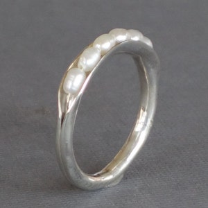 May include: A silver ring with a row of white pearls set into the band.