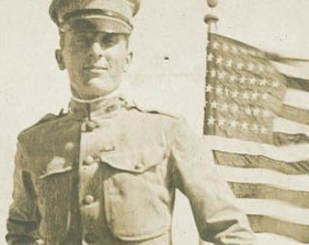 Foto antigua de 1918. Apuesto soldado estadounidense con uniforme de infantería de marina en la cubierta de un barco con bandera estadounidense. RPPC 54 E