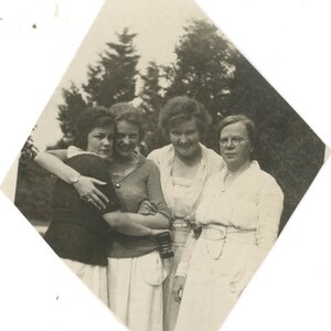 Puede incluir: Cuatro mujeres se paran juntas en una foto en blanco y negro. Todas sonríen y parecen ser amigas. Las mujeres visten vestidos y están de pie en un entorno de jardín.