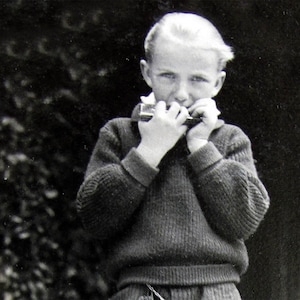 Può includere: Un giovane con un maglione grigio suona l'armonica. La persona sta guardando l'armonica e ha le mani che coprono lo strumento.