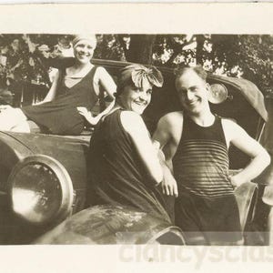 Könnte beinhalten: Schwarz-Weiß-Fotografie von drei Personen, die mit einem Oldtimer posieren. Zwei Frauen und ein Mann lächeln in die Kamera. Der Mann trägt ein gestreiftes Tanktop. Das Auto hat ein Nummernschild mit der Nummer 583.