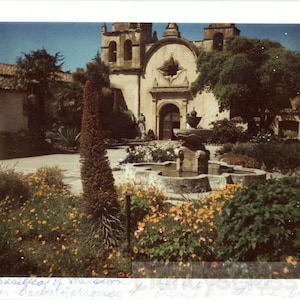 May include: A vintage postcard featuring a photo of the Basilica of Mission San Carlos Borromeo de Carmelo in Carmel, California. The photo shows the front of the church with a fountain in the foreground and a garden with flowers.