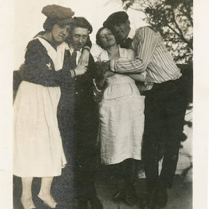 May include: A black and white photo of four people standing together. Two women are wearing white dresses and two men are wearing dark suits. The women are smiling and the men are looking at the camera.