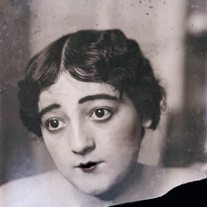 May include: A black and white portrait of a woman with dark hair styled in waves. She is looking up and to the left, with a slightly surprised expression on her face.