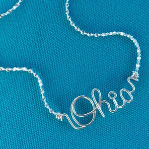 Può includere: Una collana d'argento con una catena di cristalli trasparenti e un ciondolo con il nome "Olivia" in filo d'argento.