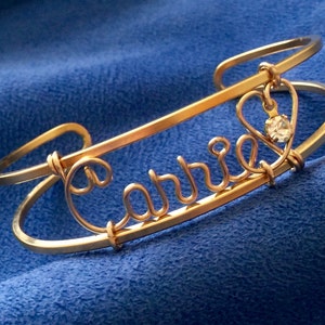 May include: Gold wire name bracelet with the name "Cabbie" and a small heart charm with a clear rhinestone.