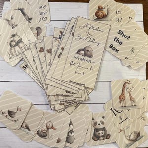 May include: A collection of beige cards with animal illustrations and text. The cards feature a variety of animals, including zebras, giraffes, pandas, and ducks. Some cards have text that reads "A Mother's Love Box Challenge" and "Shut the Box."