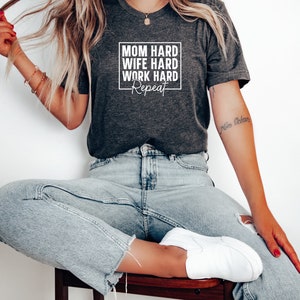 May include: A dark grey t-shirt with a white graphic that says "Mom Hard Wife Hard Work Hard Repeat".