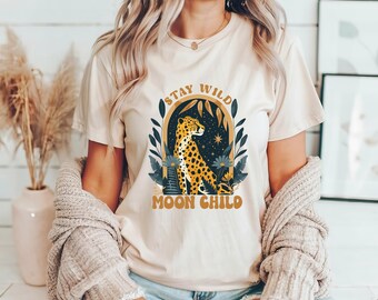 May include: A cream colored t-shirt with a graphic of a leopard in a floral frame. The text "Stay Wild Moon Child" is printed on the shirt.