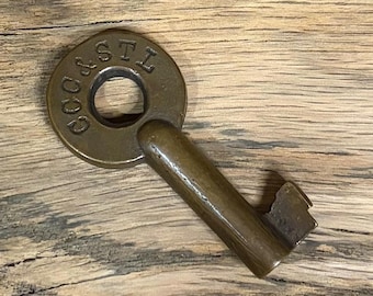 May include: A brass-colored metal key featuring a circular bow with the embossed text "CC & STL" around the center hole. The key has a cylindrical shank and a simple, notched bit at the end, displaying a smooth, aged metallic finish throughout.
