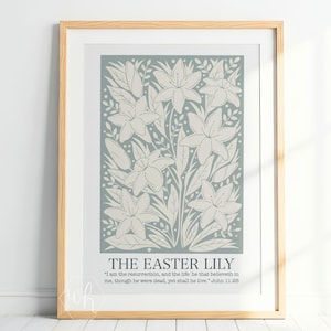 Puede incluir: Un estampado enmarcado con un diseño floral de lirios de Pascua en tonos crema y verde. La obra de arte incluye el texto "THE EASTER LILY" y un versículo bíblico. El estampado está enmarcado en un marco de madera clara.