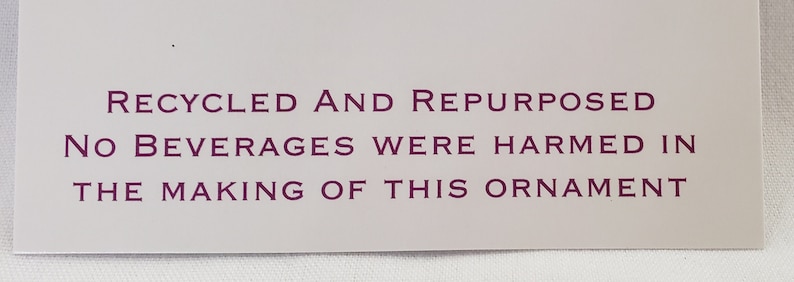 May include: Recycled and repurposed ornament with the text "Recycled and Repurposed No Beverages Were Harmed in the Making of This Ornament".