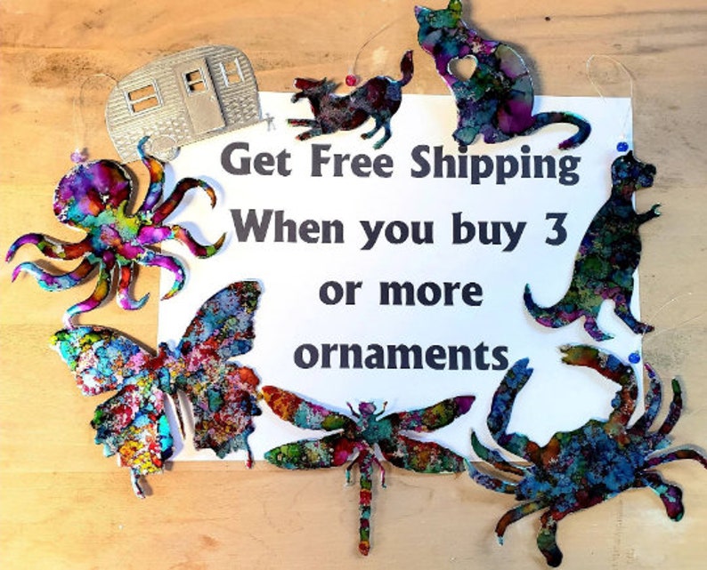 May include: A collection of colourful metal ornaments, including a butterfly, dragonfly, octopus, crab, dinosaur, cat, and a camper. The ornaments are hanging from strings and have a watercolour-like paint finish. The text "Get Free Shipping When you buy 3 or more ornaments" is written on a white background.