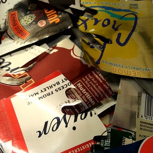 May include: A close-up of a pile of crushed aluminium cans, including a red can with the word "Red Bull" and a yellow can with the words "Naturally Essenced Lemon Croix".