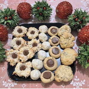May include: A platter of assorted Christmas cookies, including chocolate chip, peanut butter, and coconut macaroons. The cookies are arranged on a black platter and surrounded by red and green Christmas ornaments.