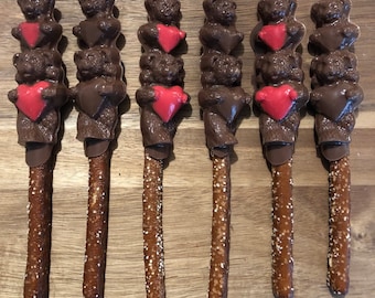 May include: Six chocolate-covered pretzel sticks with three chocolate bears and a red heart on each stick. The bears are stacked on top of each other.