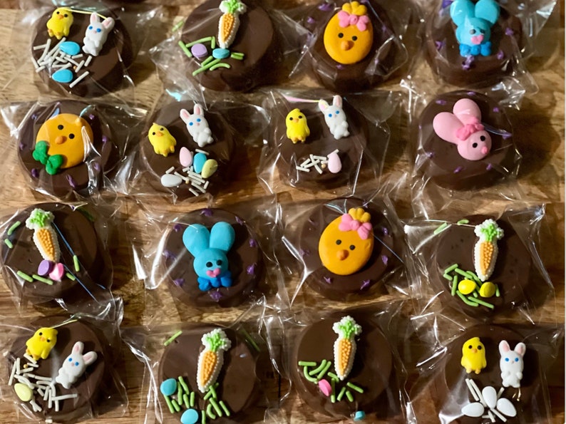 Puede incluir: Galletas cubiertas de chocolate decoradas con caramelos tem&aacute;ticos de Pascua. Cada galleta est&aacute; envuelta individualmente y presenta dise&ntilde;os coloridos de conejitos, pollitos y zanahorias, junto con chispas y huevos de colores pastel. Un dulce festivo para las fiestas.
