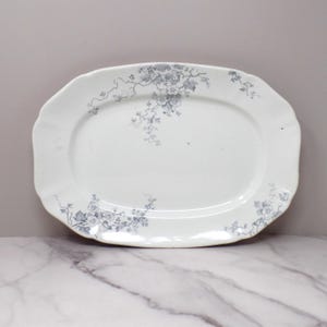 May include: Oval white serving platter with a scalloped edge. The platter features a delicate blue floral vine pattern around the rim. The serving dish is ideal for displaying food.