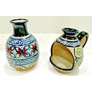 May include: Two small ceramic vases with intricate blue, white, red, and green patterns. One vase has a handle and a cutout on the side, while the other is a round vase.