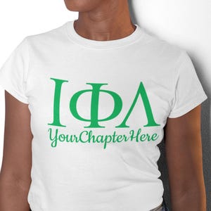 Peut inclure: T-shirt blanc avec un motif de lettres grecques vertes qui dit "IΦA" et "Your Chapter Here" en texte vert.