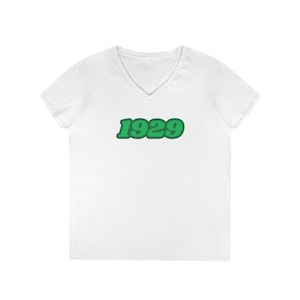 Könnte beinhalten: Weißes T-Shirt mit V-Ausschnitt und grüner 1929 Grafik.