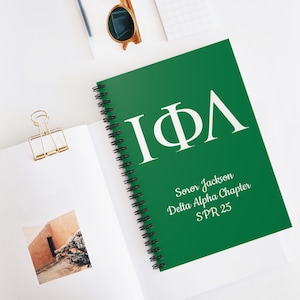 Può includere: Un quaderno a spirale verde con le lettere greche "IΦΛ" in bianco. Il testo "Soror Jackson Delta Alpha Chapter SPR 25" è stampato sotto le lettere.