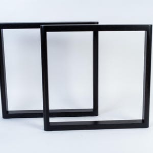 May include: Two black, rectangular table legs. The legs are made of solid wood and have a modern, minimalist design. The legs are shown against a white background.
