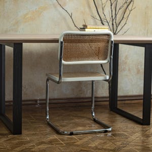 May include: A light wood desk with black legs and a white chair with a woven back. The chair has a chrome frame. A small stack of books sits on the desk.