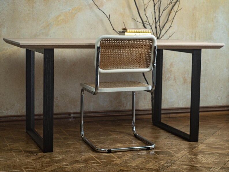 May include: A light wood desk with black legs and a white chair with a woven back. The chair has a chrome frame. A small stack of books sits on the desk.
