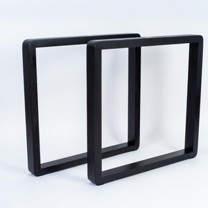 May include: Two black, square-shaped table legs. The legs are made of solid wood and have a smooth, matte finish. The design is modern and minimalist, suitable for various furniture projects. The legs are shown against a white background.