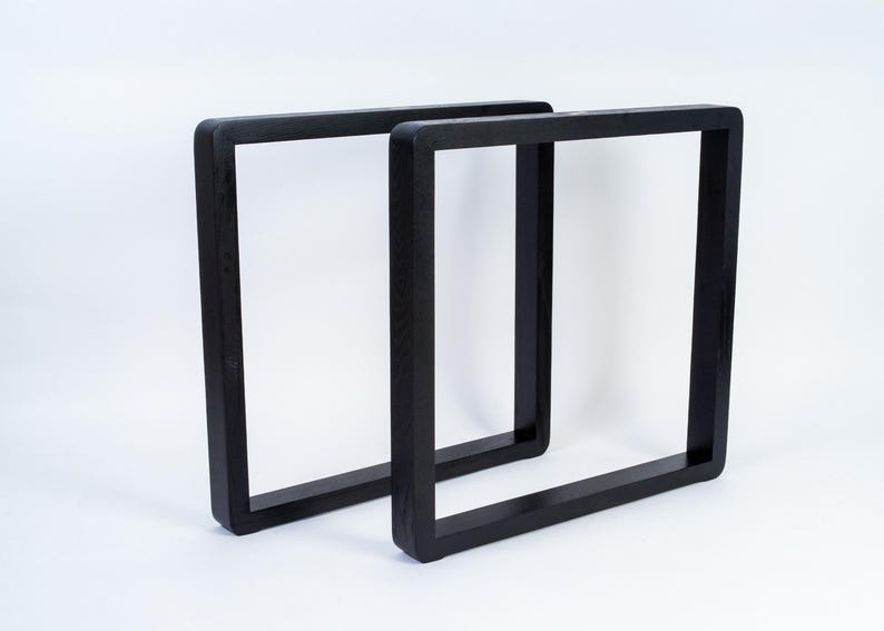 May include: Two black, square-shaped table legs. The legs are made of solid wood and have a smooth, matte finish. The design is modern and minimalist, suitable for various furniture projects. The legs are shown against a white background.