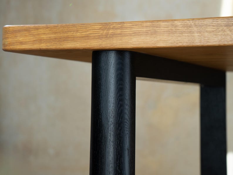 May include: Close-up of a wooden table with a light brown tabletop and black legs. The tabletop has a natural wood grain, and the legs are cylindrical. The table is likely for a living room or dining room.