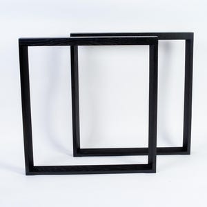 May include: Two black wooden picture frames, rectangular in shape, are displayed against a white background. The frames are empty, with a simple, modern design. The frames are likely for displaying art or photographs.
