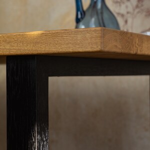 May include: Close-up of a wooden table with a light brown top and black legs. The table has a rectangular shape and a natural wood grain finish. A blue decorative vase is on the table.