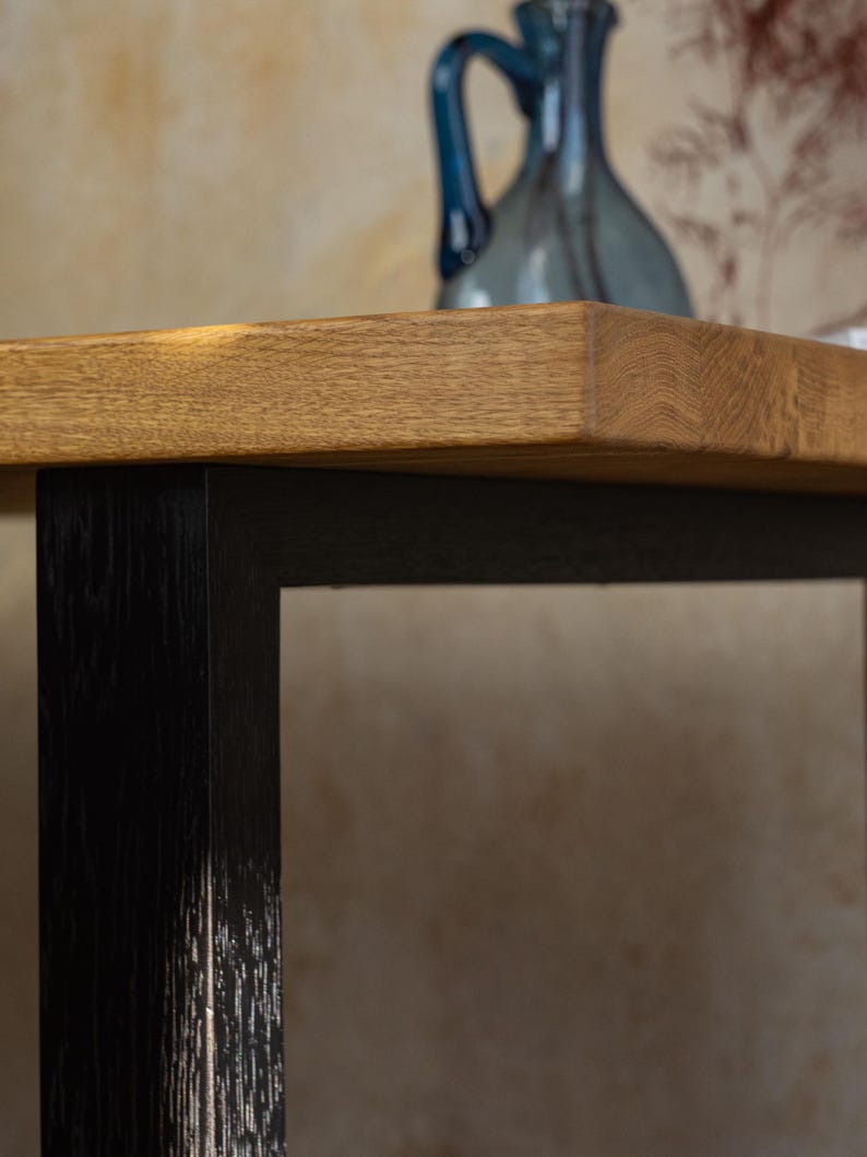 May include: Close-up of a wooden table with a light brown top and black legs. The table has a rectangular shape and a natural wood grain finish. A blue decorative vase is on the table.