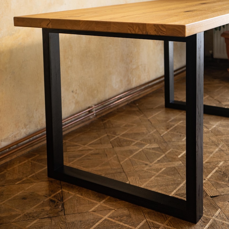 May include: A wooden table with a light brown tabletop and black metal legs. The table has a rectangular shape and is supported by four square legs. The tabletop appears to be made of solid wood.
