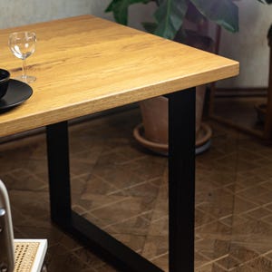May include: A rectangular wooden table with a light brown finish and black metal legs. A wine glass and black plate are on the table. The table's dimensions are not visible in the image.