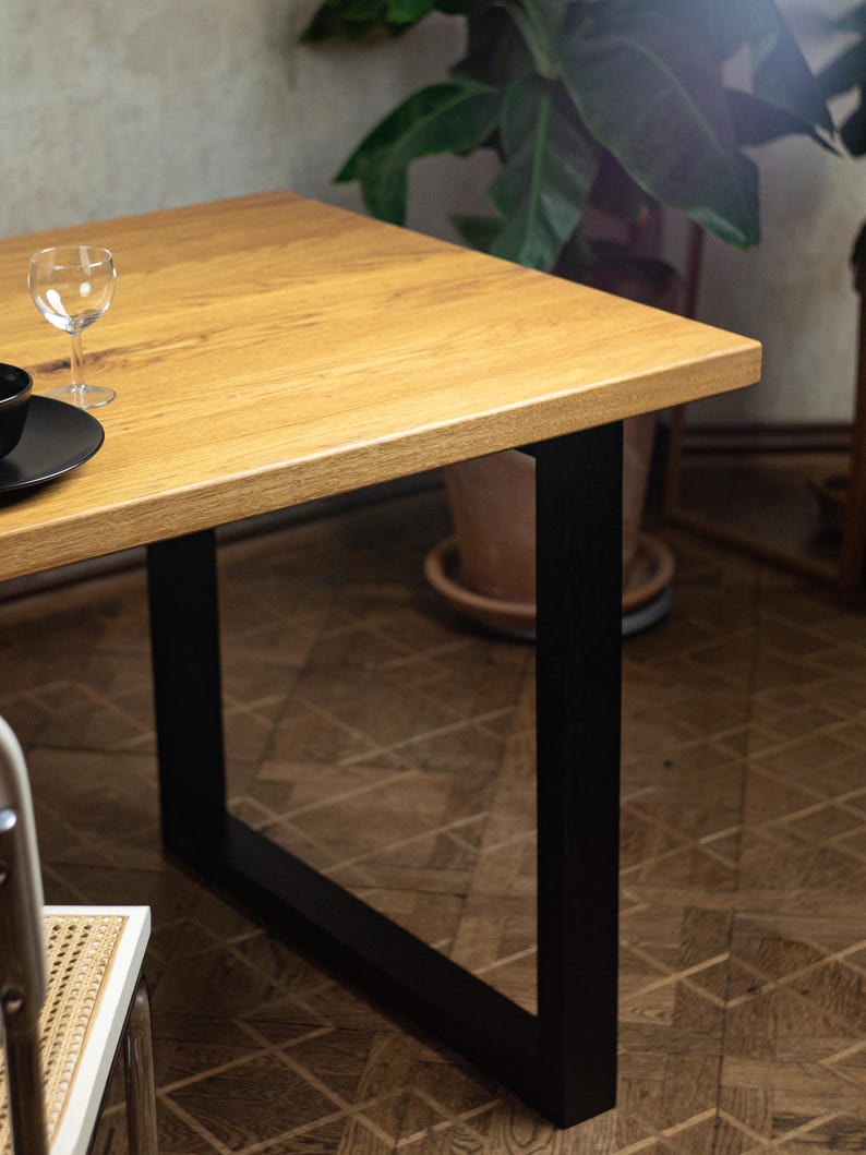 May include: A rectangular wooden table with a light brown finish and black metal legs. A wine glass and black plate are on the table. The table's dimensions are not visible in the image.