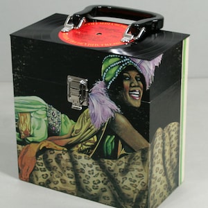 May include: A black vinyl record storage box featuring a portrait of a woman in a turban and leopard print fabric. The box has a black handle and silver hardware. A red record label is visible on top.