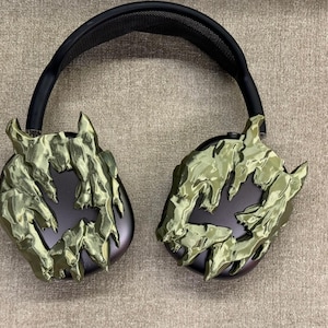 May include: Black headphones with a green camouflage pattern on the earcups. The pattern resembles a rocky, mountainous terrain.