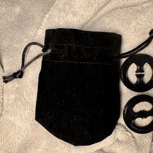 以下が含まれることがあります： 黒いベルベットの巾着袋に入った黒いプラスチック製のブラクリップ2個。クリップは8の字型です。