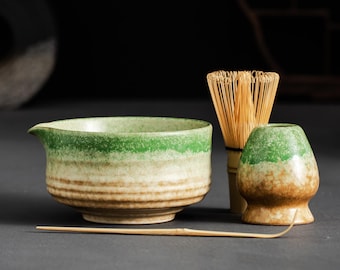 May include: A matcha tea set featuring a green and beige ceramic bowl with a spout, a bamboo whisk, a small ceramic holder, and a bamboo spoon. The set has a rustic, handcrafted appearance, perfect for tea ceremonies.