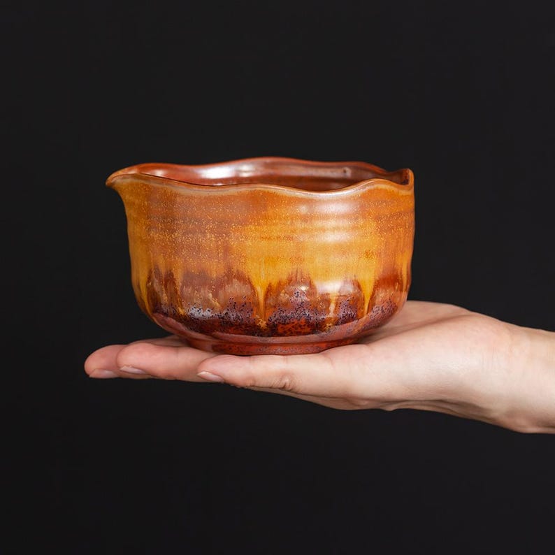 May include: A small ceramic bowl with a wavy, scalloped rim. The exterior features a gradient glaze transitioning from a warm, golden-yellow at the top to a deep, rich reddish-brown at the base, with visible drip patterns throughout the surface.