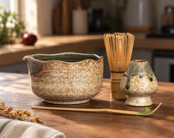 May include: A ceramic matcha bowl with a speckled tan and green glaze, a bamboo whisk, a ceramic whisk holder with a matching speckled finish, and a long bamboo tea scoop with a small amount of green matcha powder on the tip of the spoon.