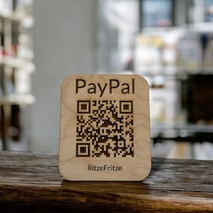 Könnte beinhalten: Ein Holzschild mit einem schwarz-weißen QR-Code und dem Text "PayPal" und "RitzFritze".