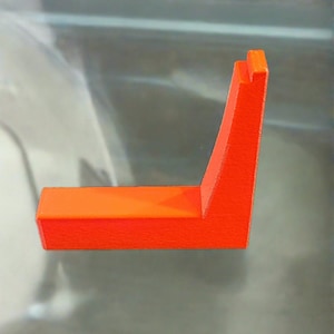 May include: A bright orange plastic L-shaped stand. The stand is made of a textured plastic and has a smooth, flat surface.