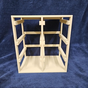 Może przedstawiać: Kremowy, otwarty regał o prostokątnym kształcie. Jednostka posiada wiele poziomych półek i pionowych podpór, tworząc strukturę przypominającą kratę. Projekt jest prosty i nowoczesny, odpowiedni do eksponowania przedmiotów.