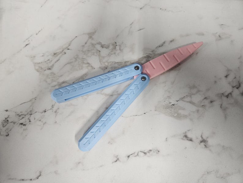 May include: A blue and pink plastic butterfly knife. The knife is closed and has a textured design.